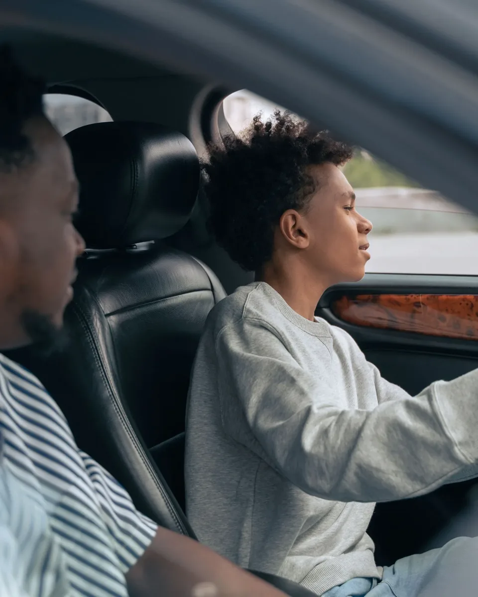 Un adolescent tient le volant, son père assis à côté de lui le guide en souriant